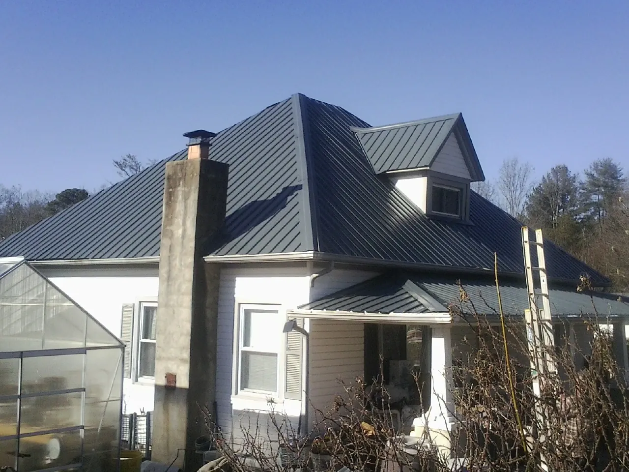 Dark blue standing seam metal roof on a white farmhouse with dormer — Slate & Tile Roof Repair by Roofing Brothers in Aultman