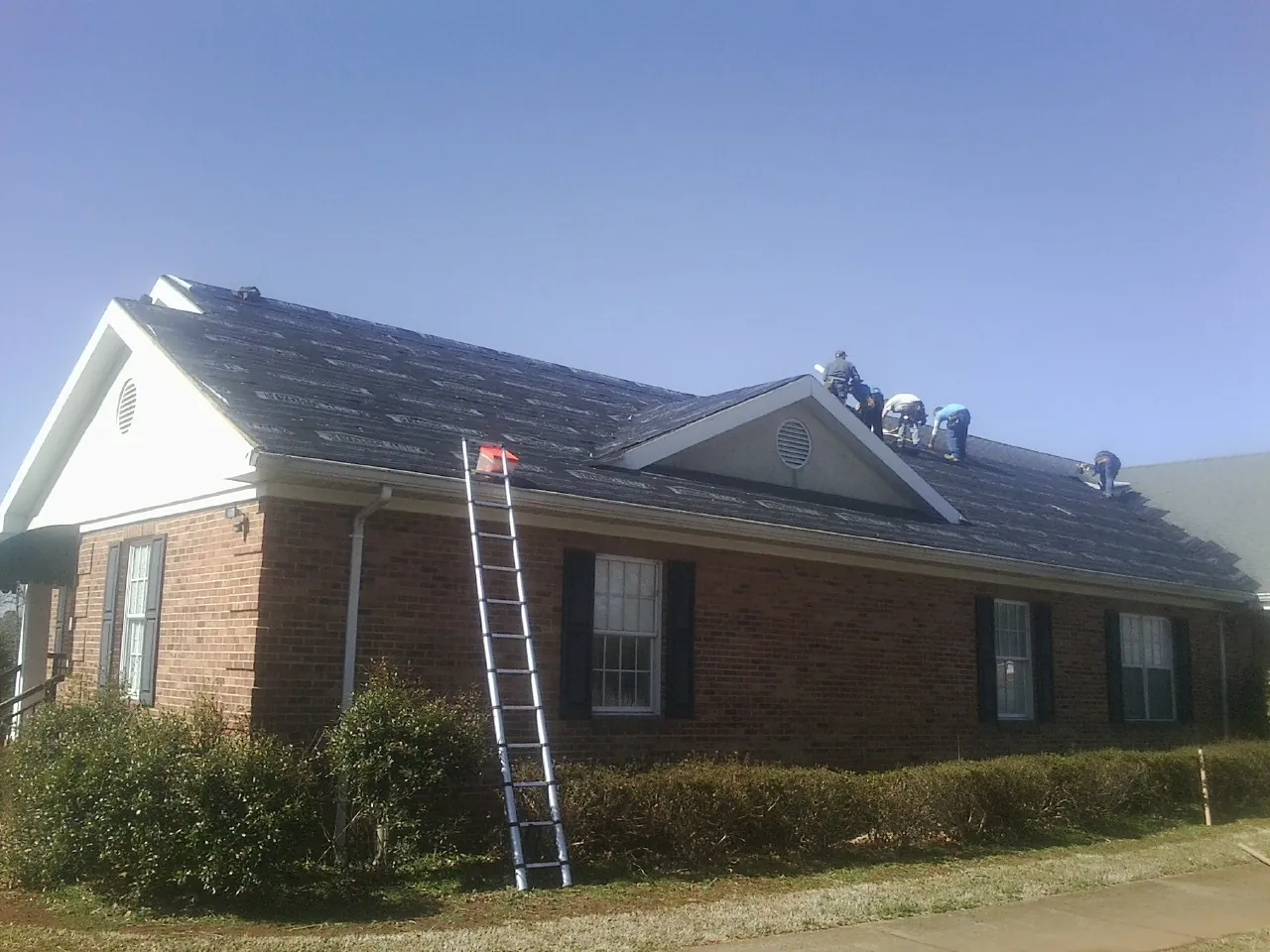 Crew tearing shingles off a brick ranch roof with a ladder set — Metal Roof Repair work by our crew in Aultman
