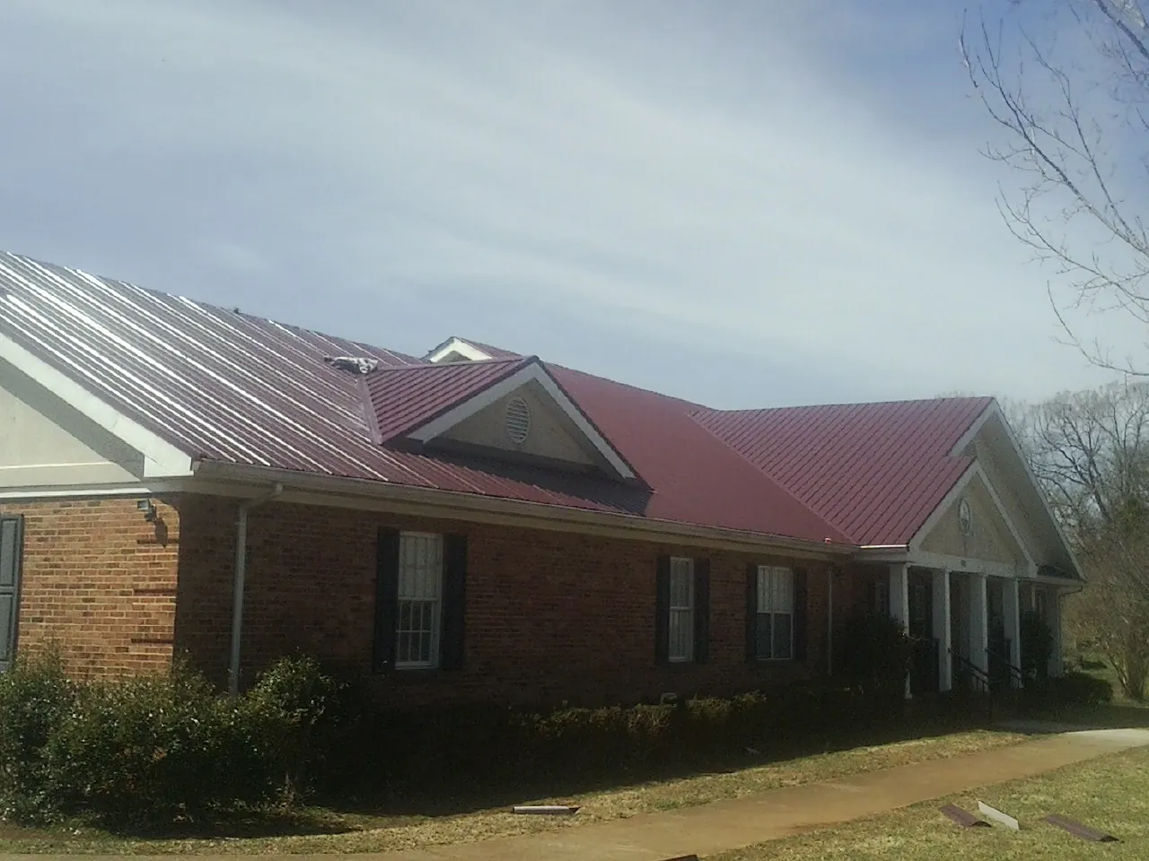 Red metal roof with gabled entries on a long brick building, from a Hail Damage Roof Repair job in Aultman