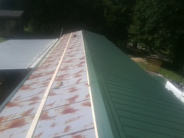 Old rusted panels beside newly installed green metal roofing — Wind Damage Roof Repair by Roofing Brothers in Aultman