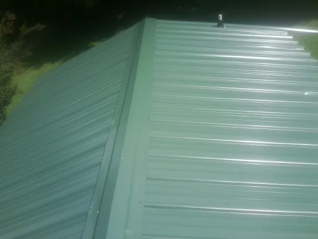 New green metal panels meeting at the ridge of a roof — Flat Roof Repair work by our crew in Aultman