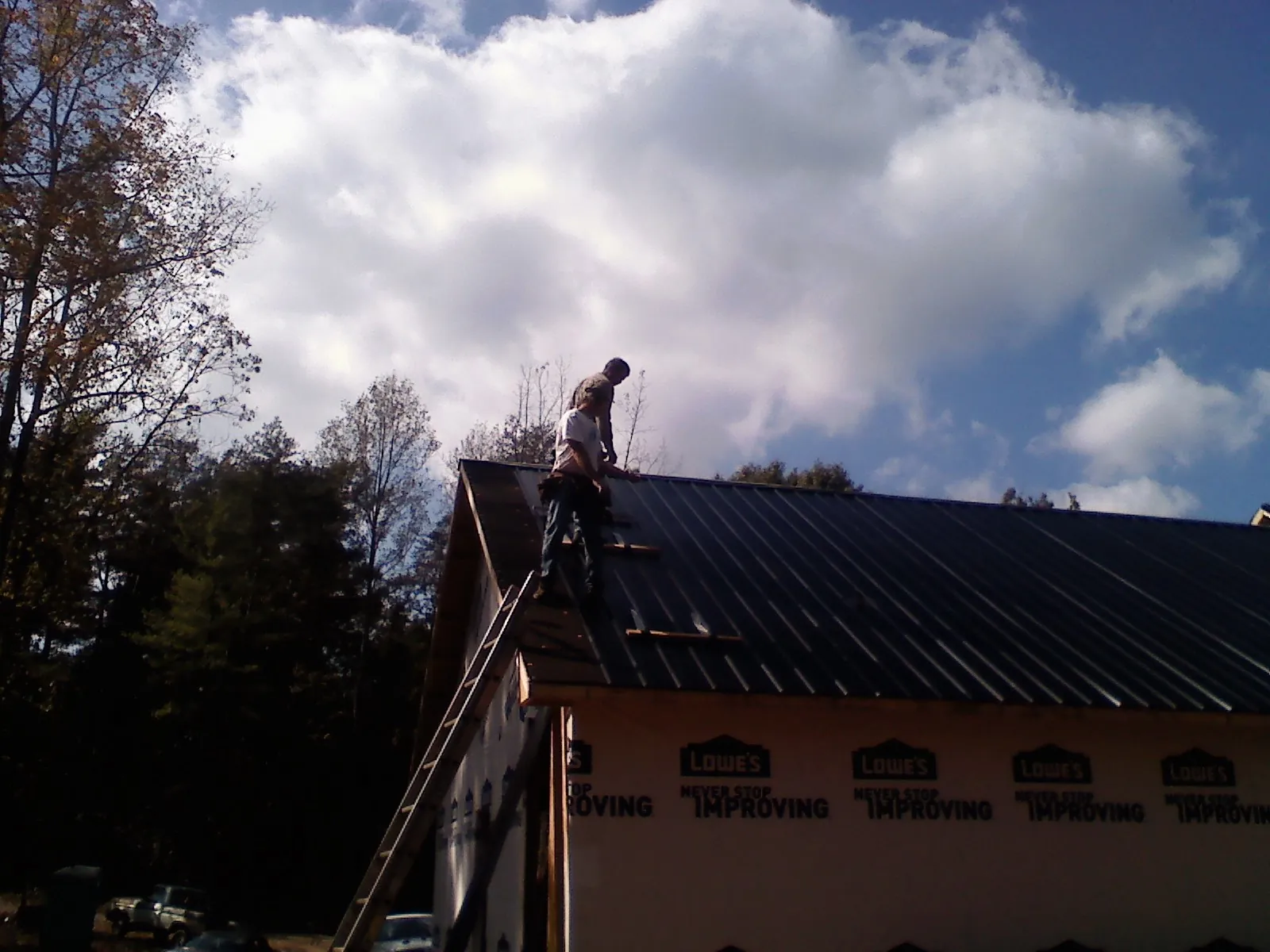 Roofer fastening dark metal panels high against a cloudy sky, from a Roof Inspection job in Aultman