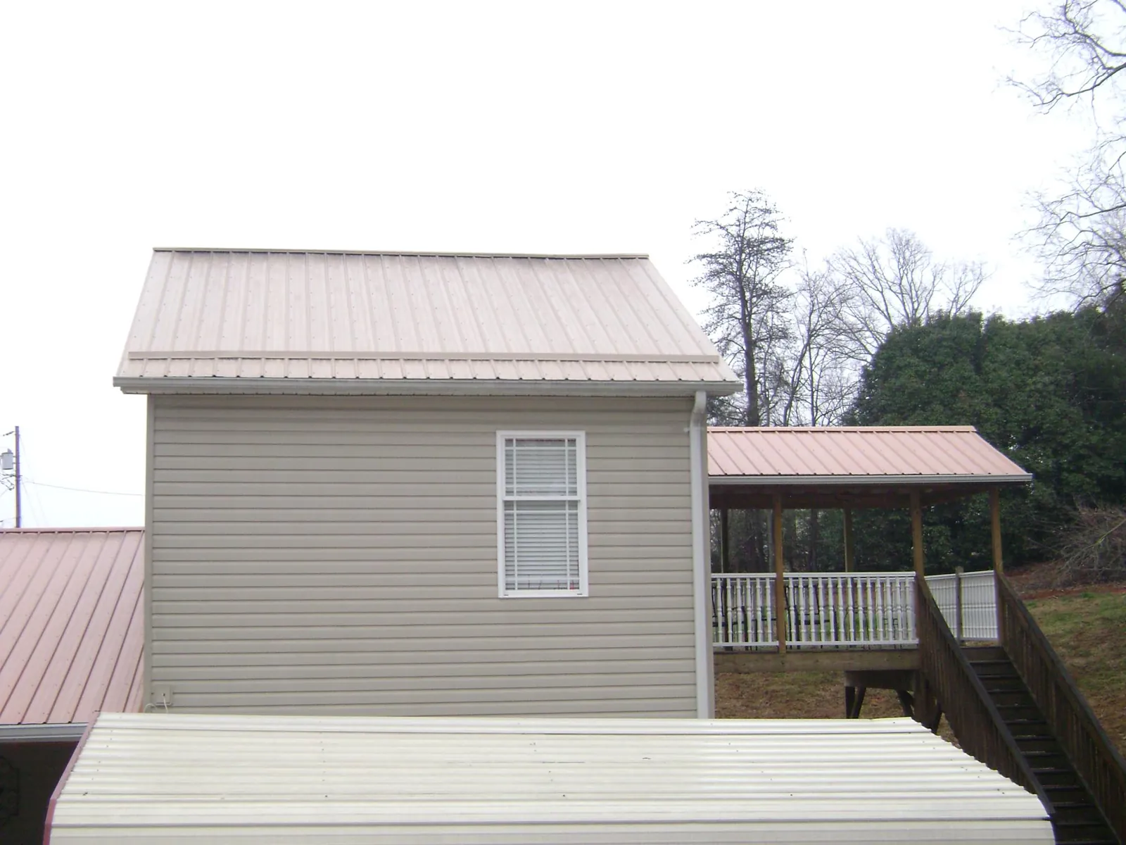 Tan metal roofs on a two story addition and attached porch, from a Roof Replacement job in Aultman